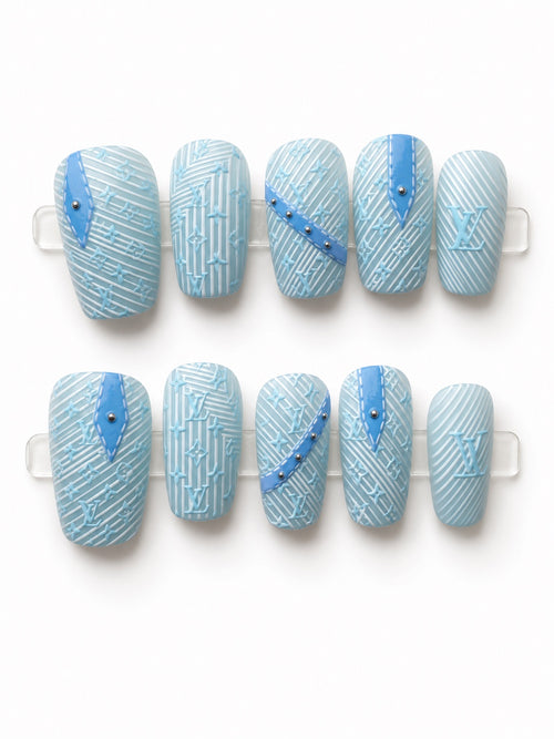 Medium light blue square press-on nails with textured monogram-inspired pattern and stud accents