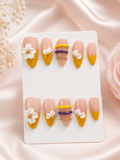 Golden Bloom Stack small almond press-on nail set with nude, mustard yellow, white floral, purple, and gold details