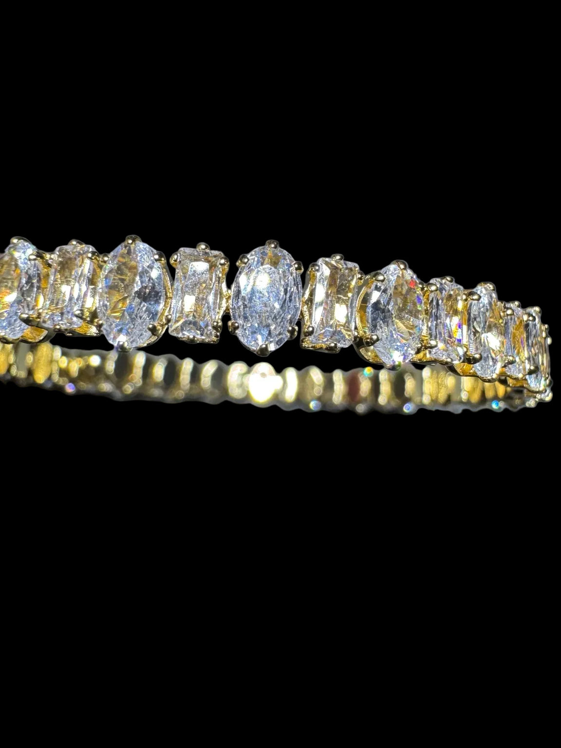 Close-up of alternating oval and emerald-cut clear stones in gold-tone setting